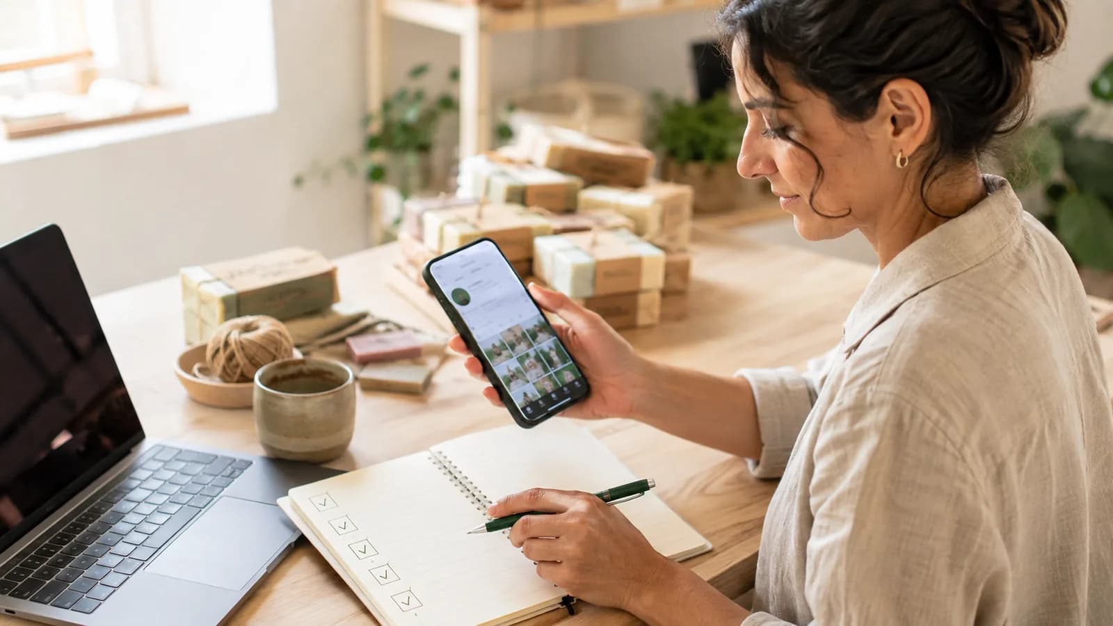 Pessoa conferindo um perfil no celular e um checklist de compra ao lado do notebook